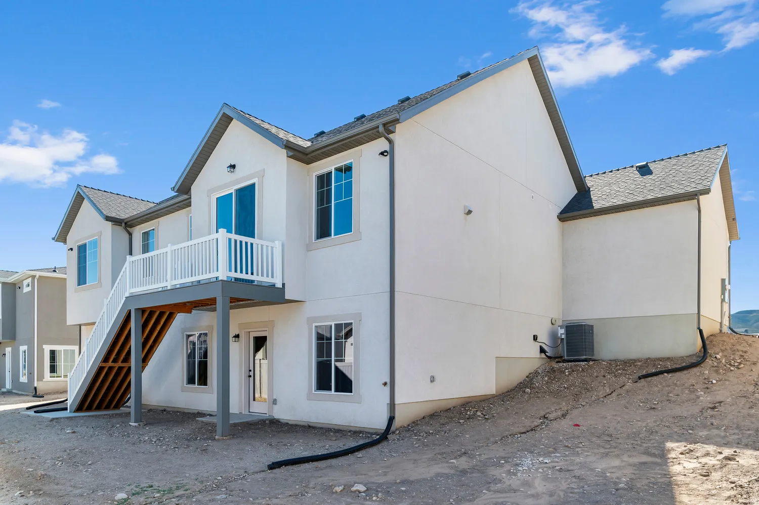 Exterior featuring a white stucco finish, a deck with white railings, a sliding glass door, multiple windows with white trim, and a shingled roof