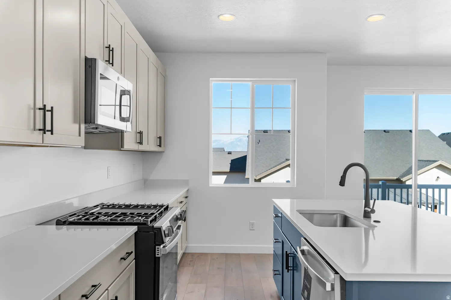 Kitchen featuring light-toned cabinetry, stainless steel microwave, gas range, and wood-finish flooring
