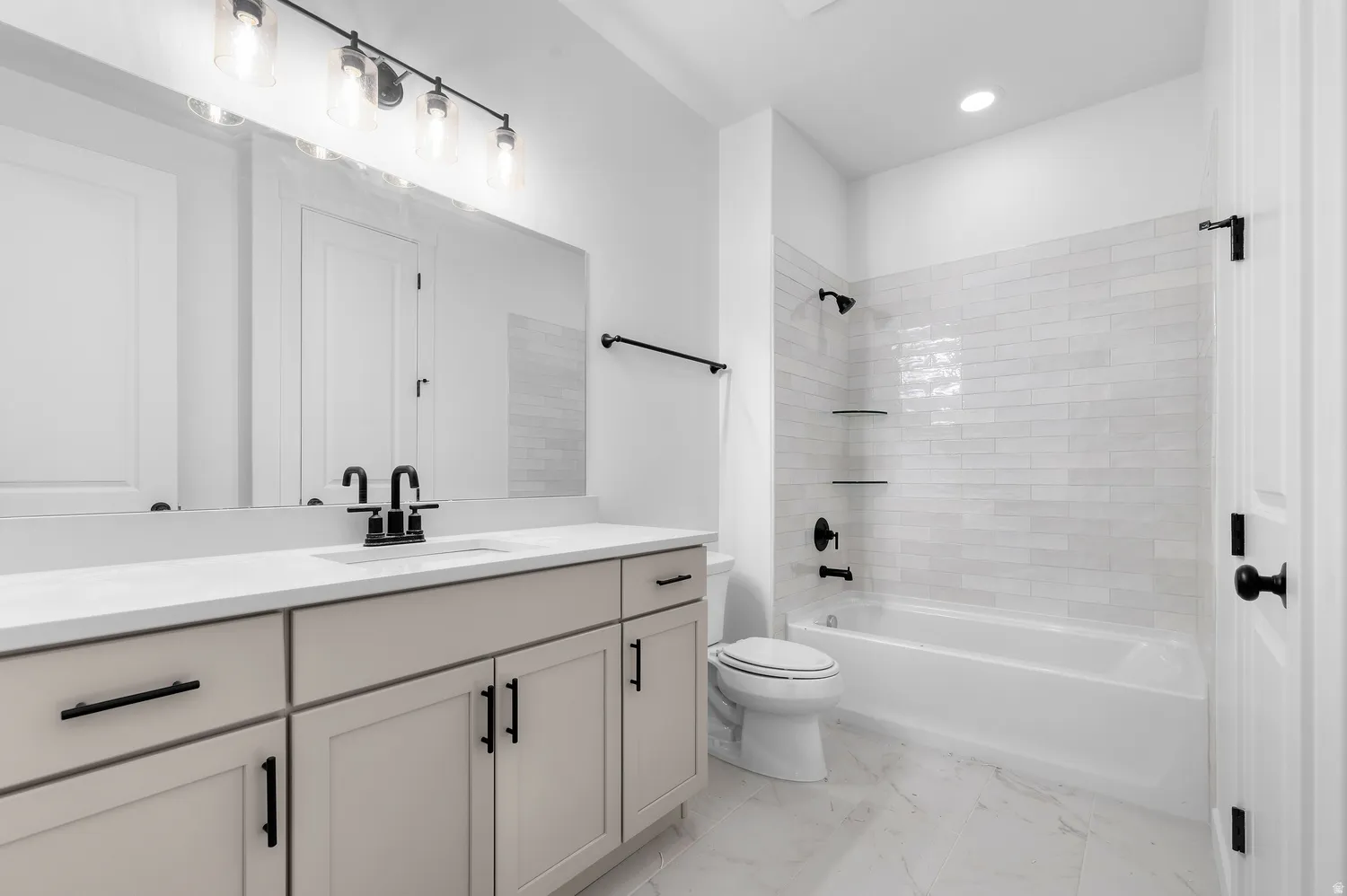 Double vanity with integrated sink, matte black fixtures, full-width mirror, subway tile bath surround, and recessed lighting