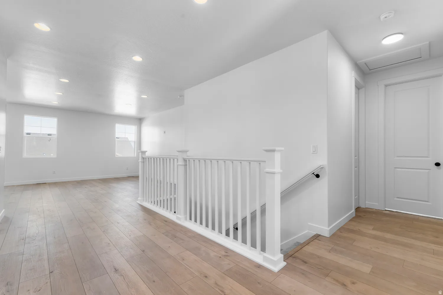 Recessed ceiling lighting, wood-finish flooring, white painted walls, white spindle railing, and a white paneled door