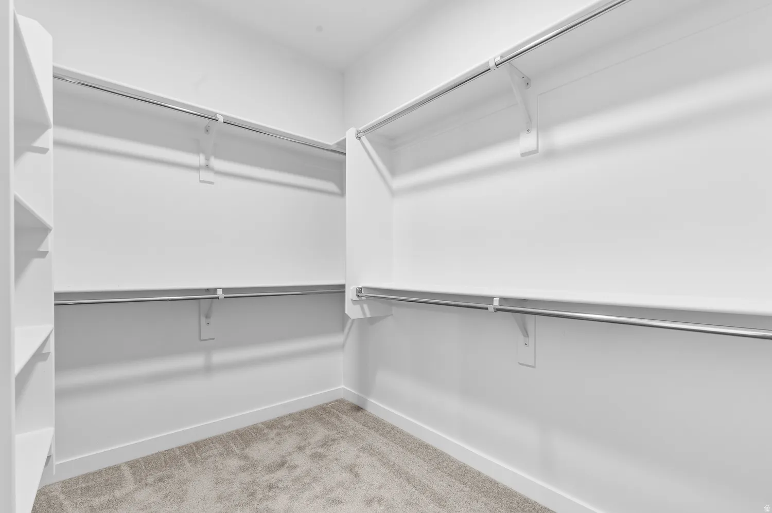 Walk-in closet with integrated shelving, multiple chrome hanging rods, and light-toned carpet flooring