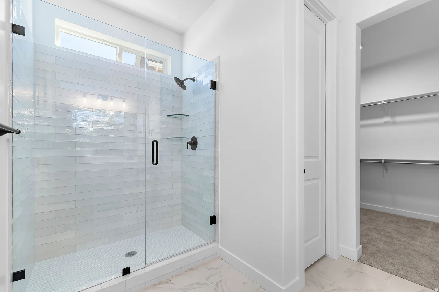 Glass-enclosed shower with subway tile surround, matte black fixtures, and a transom window