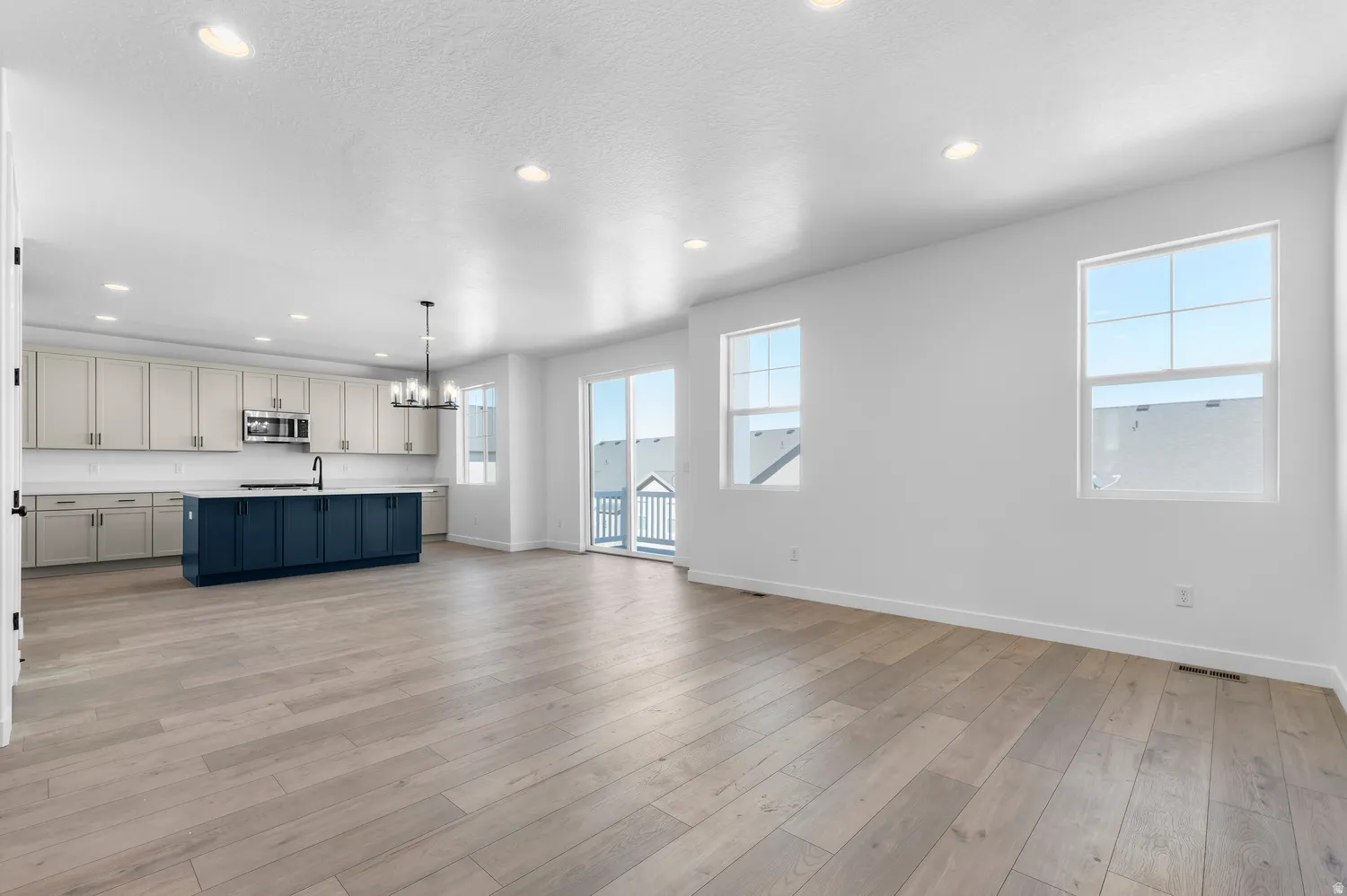Bright, open-concept living space with wood-finish flooring, recessed lighting, and a sliding glass door