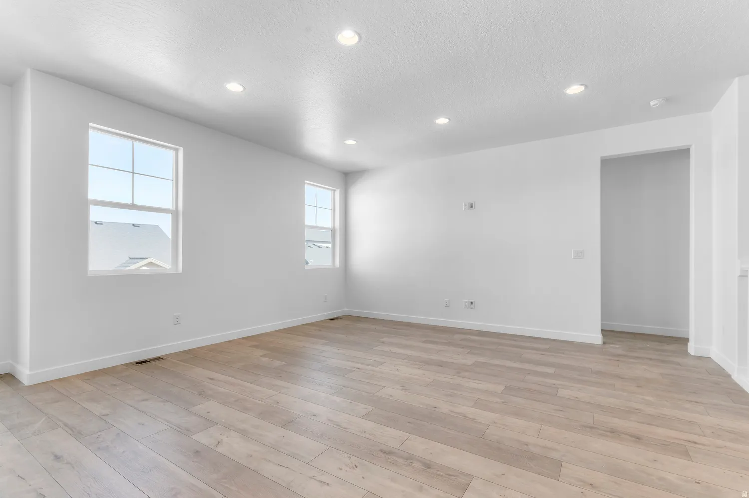 Recessed lighting, light wood-finish flooring, two large windows, white walls, and a spacious open-concept room