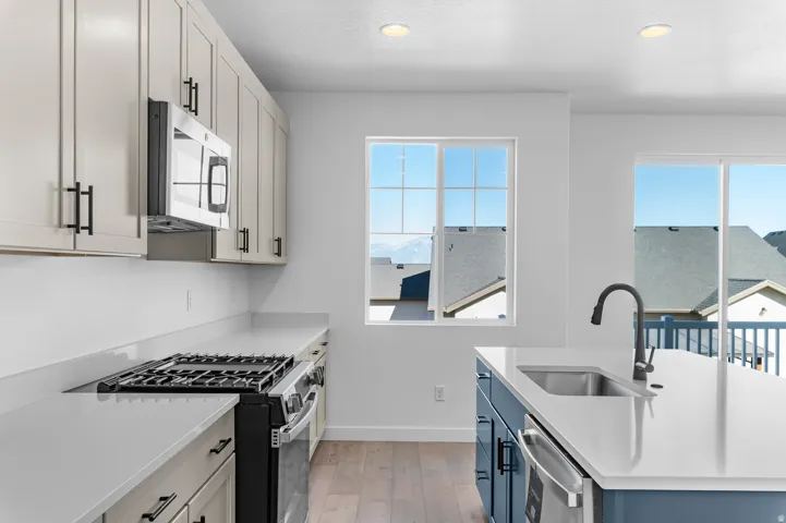 Kitchen featuring light-toned cabinetry, stainless steel microwave, gas range, and wood-finish flooring