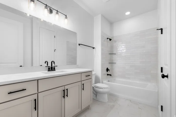 Double vanity with integrated sink, matte black fixtures, full-width mirror, subway tile bath surround, and recessed lighting