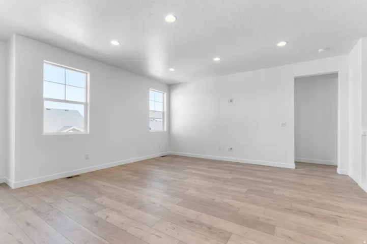 Recessed lighting, light wood-finish flooring, two large windows, white walls, and a spacious open-concept room