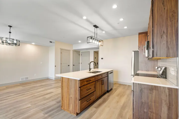 Gourmet kitchen featuring a substantial wood-finish island with integrated sink and prep space, white quartz countertops, stainless steel appliances, and custom cabinetry