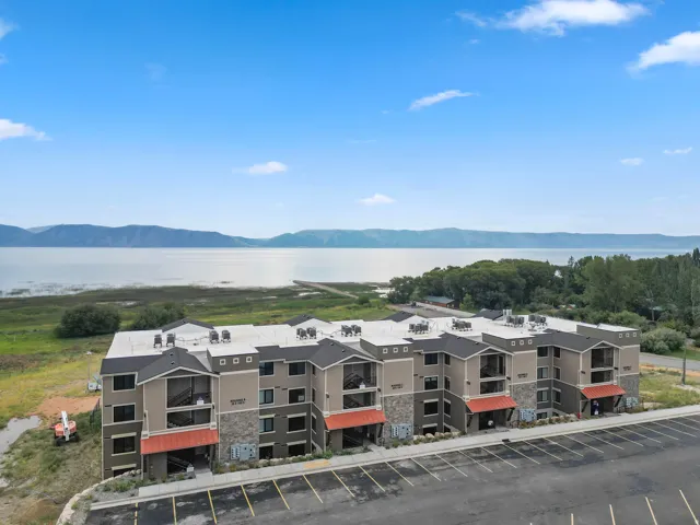 Multi-story residential building featuring a stone and siding exterior with red awnings, dark framed windows, and a paved parking area