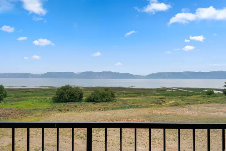 Balcony with black metal railings overlooking a lake, mountains, and natural landscaping
