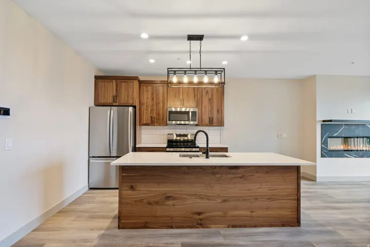 Contemporary kitchen island featuring a light-toned countertop, integrated sink with a matte black faucet, and wood-finish paneling