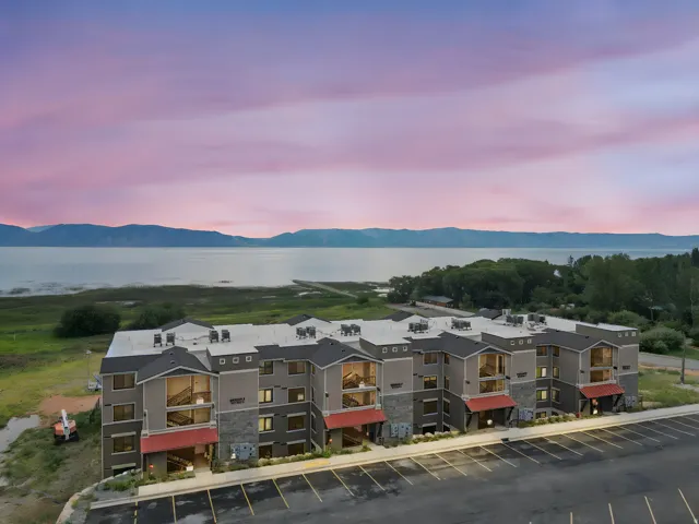 Contemporary multi-story building featuring a facade of gray siding, stone accents, and red awnings