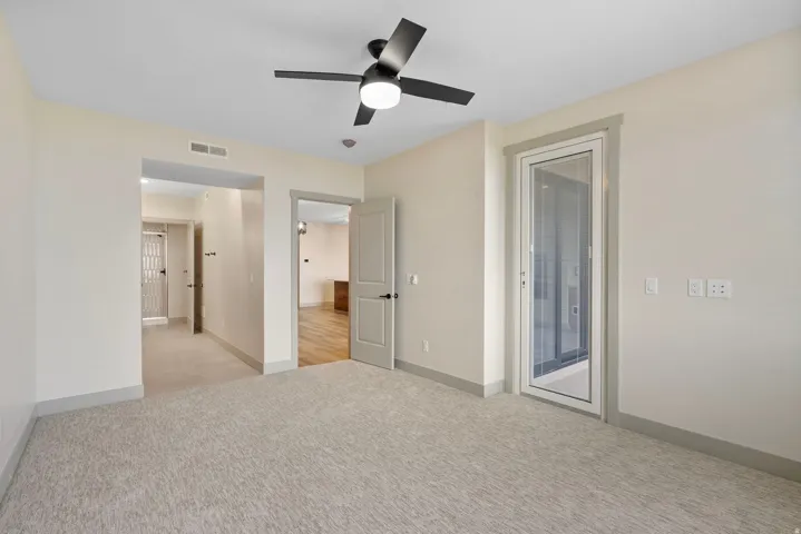 Neutral-toned room featuring light-colored carpeting, a contemporary black ceiling fan with integrated lighting, and a glass-paneled door
