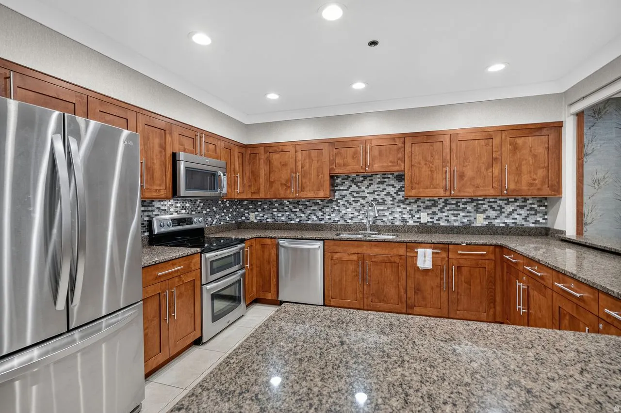 Kitchen featuring wood cabinetry, stainless steel appliances, speckled stone countertops, and a mosaic tile backsplash