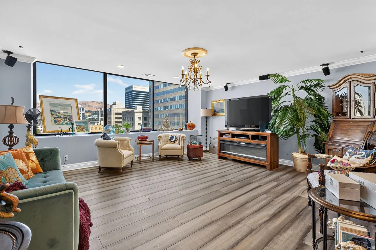 Spacious living area featuring expansive windows with city and distant mountain views, wood-finish flooring, a decorative chandelier, recessed lighting, and crown molding