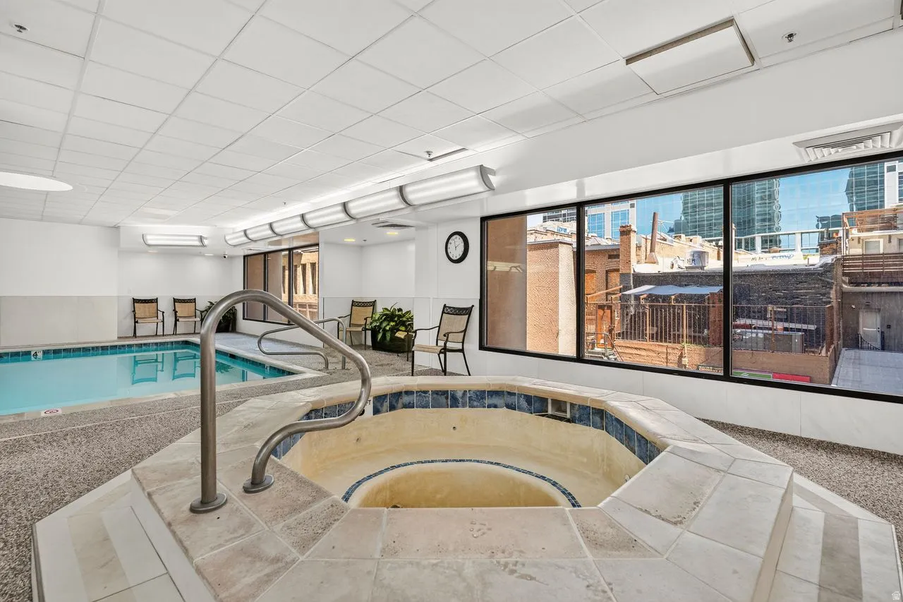 Indoor aquatic wellness center featuring a heated swimming pool with integrated spa, dual entry stairs with handrails, and expansive windows overlooking the cityscape