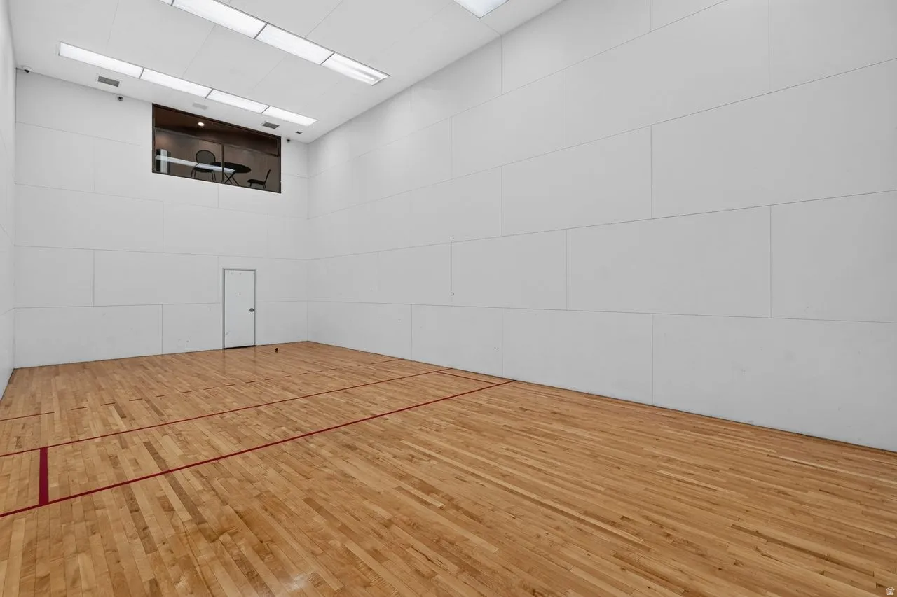 Dedicated indoor court featuring hardwood flooring with red court lines, high white panel walls, integrated ceiling lighting, and an overhead viewing window