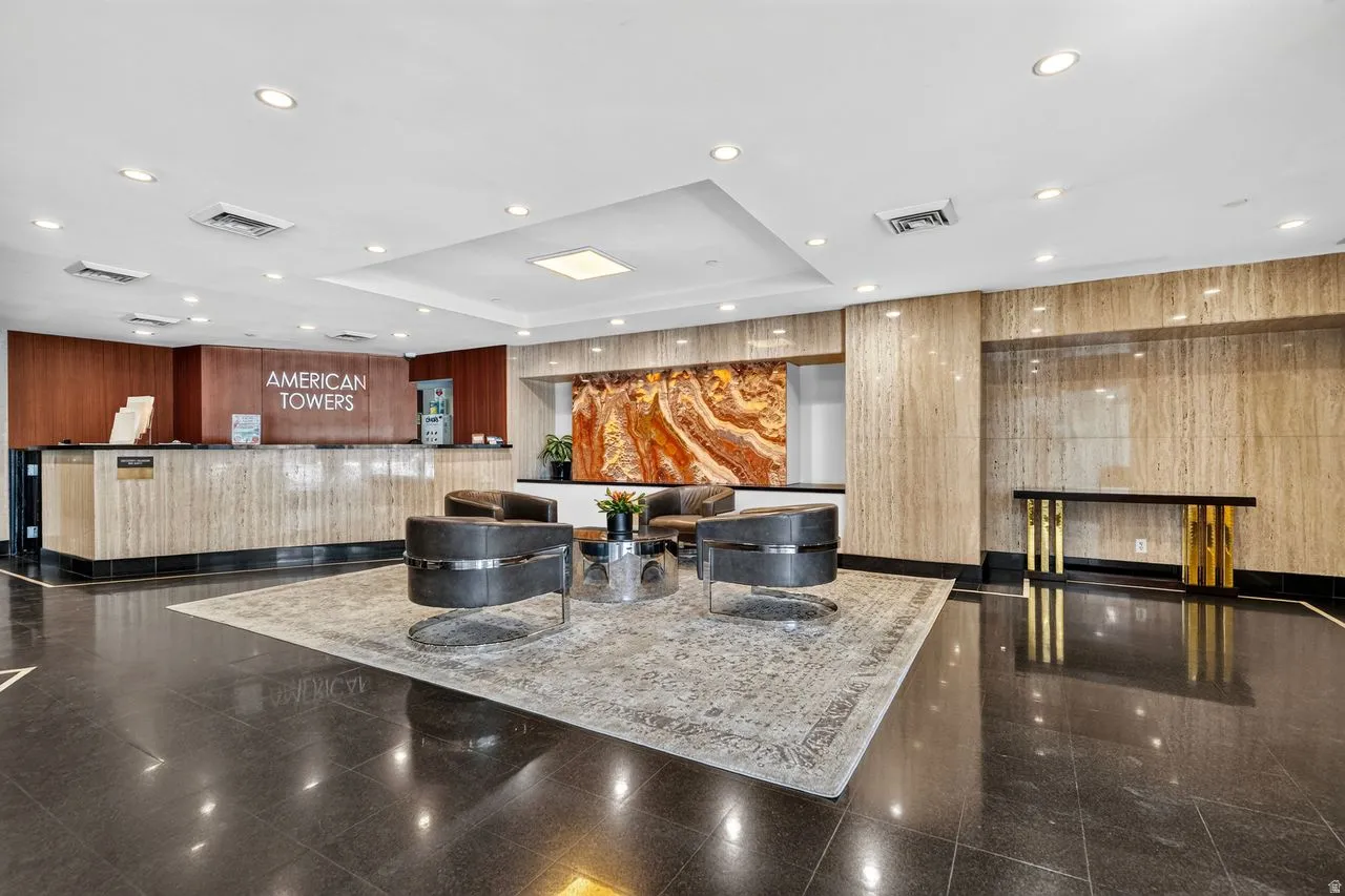 Spacious lobby featuring polished black tile flooring, recessed lighting, a reception desk with stone-finish paneling, and an accent wall with a large abstract art piece