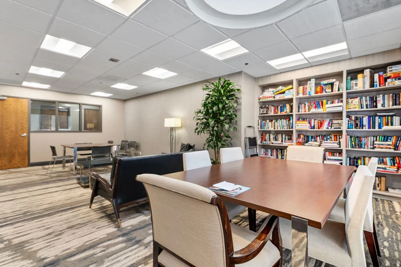 Community room featuring a full wall of built-in shelving, wood-finish tables, patterned carpet, and recessed lighting