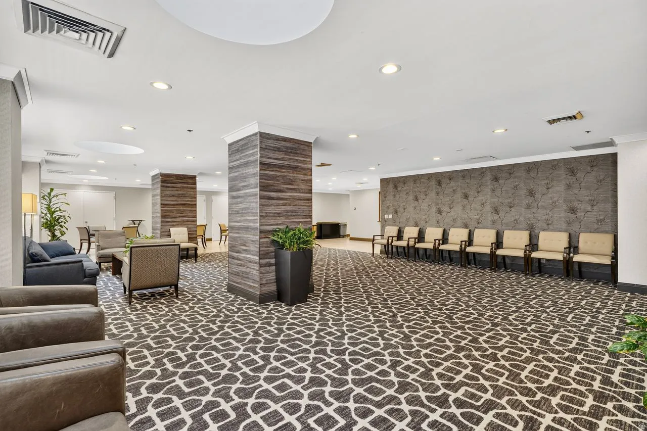 Spacious common area featuring patterned carpet flooring, recessed lighting, and support columns with wood-finish paneling