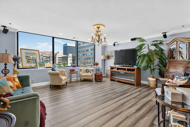 Spacious living area featuring expansive windows with city and distant mountain views, wood-finish flooring, a decorative chandelier, recessed lighting, and crown molding