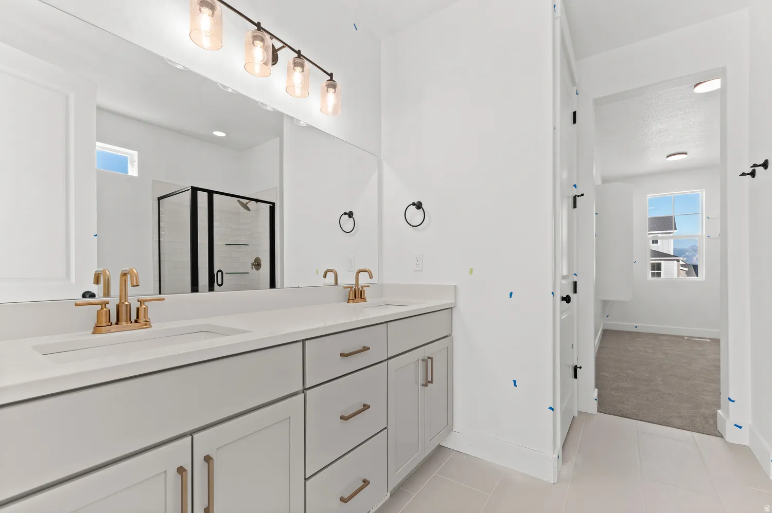 Dual vanity with integrated sinks and brass-finish fixtures, ample under-counter storage, large mirror, and glass-enclosed shower with black trim