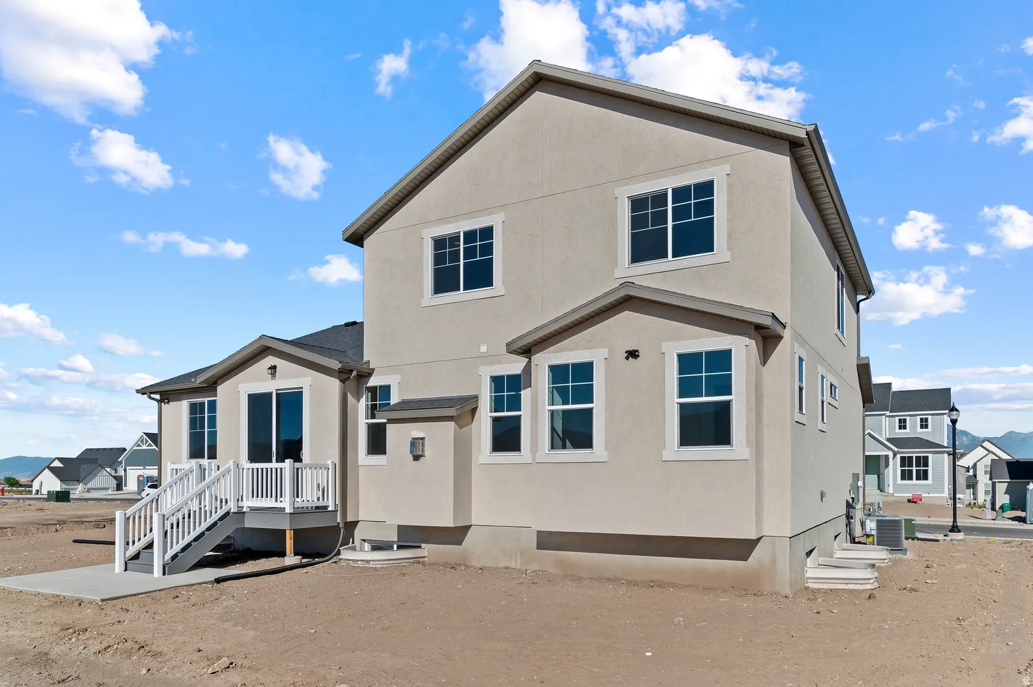 Multi-level home featuring stucco exterior, white-framed windows, a walk-out deck with white railings, and a concrete patio