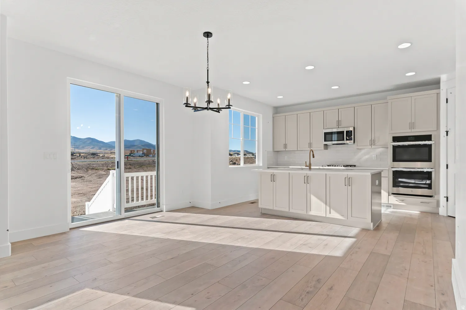 Open concept kitchen and dining space featuring wood-finish flooring, white cabinetry, a kitchen island with seating, a built-in double oven, and a sliding glass door