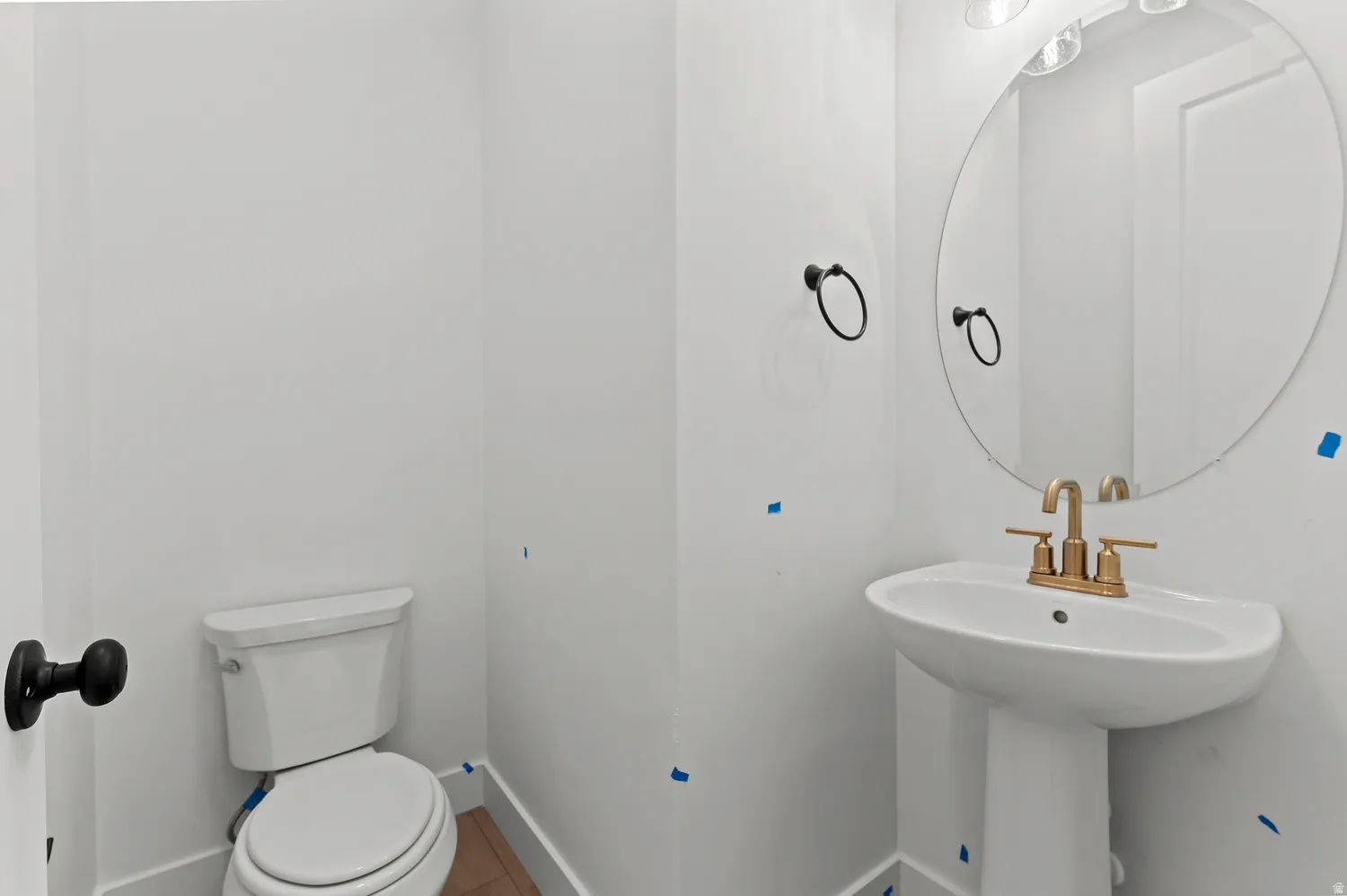 Pedestal sink with brass-finish faucet, circular mirror, and matte black hardware