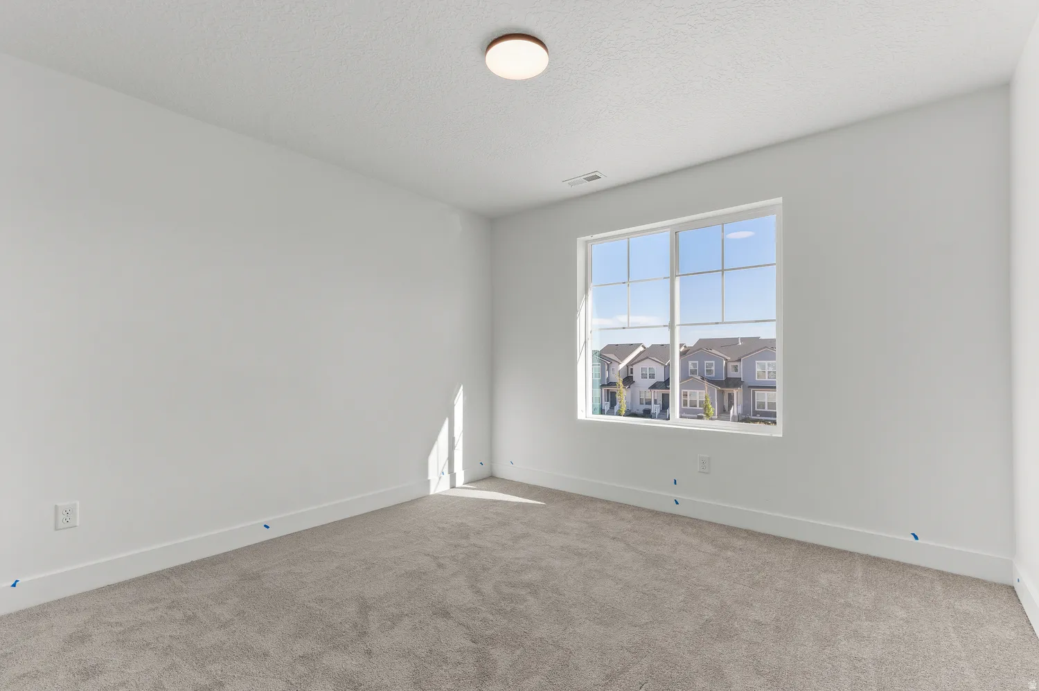 Recessed window with grid pattern, neutral gray carpeting, white walls, and a ceiling-mounted light fixture