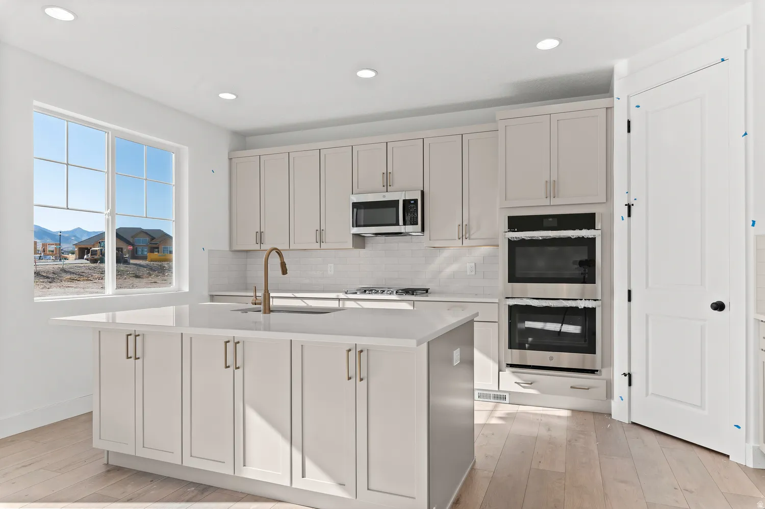 Light-filled kitchen with a central island, recessed lighting, double wall ovens, a built-in microwave, and wood-finish flooring