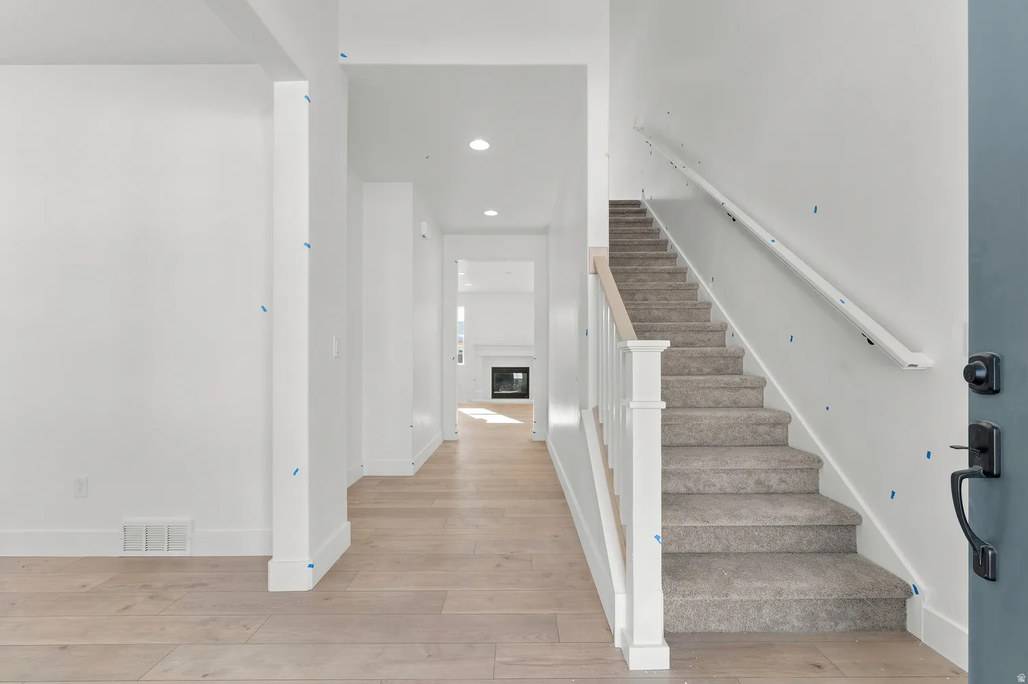Light wood-finish flooring, recessed lighting, carpeted staircase with white balusters, and a contemporary fireplace