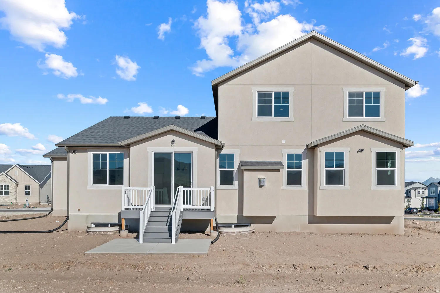 Stucco exterior, multi-pane windows, elevated deck with white railings, concrete patio, and dark shingle roof