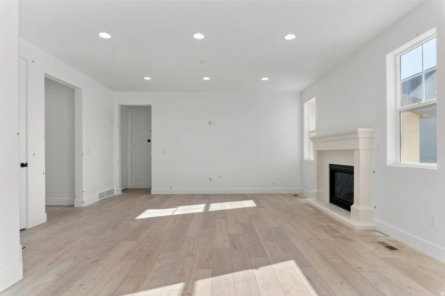 Recessed lighting, wood-finish flooring, white walls, two windows, and a built-in fireplace with a mantel