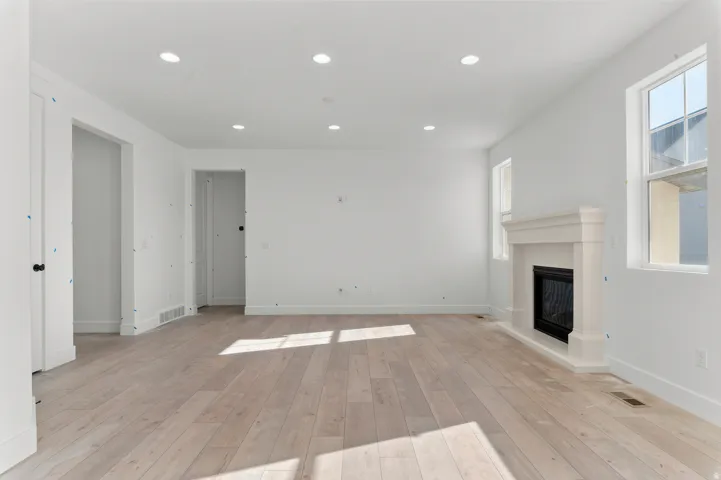 Recessed lighting, wood-finish flooring, white walls, two windows, and a built-in fireplace with a mantel