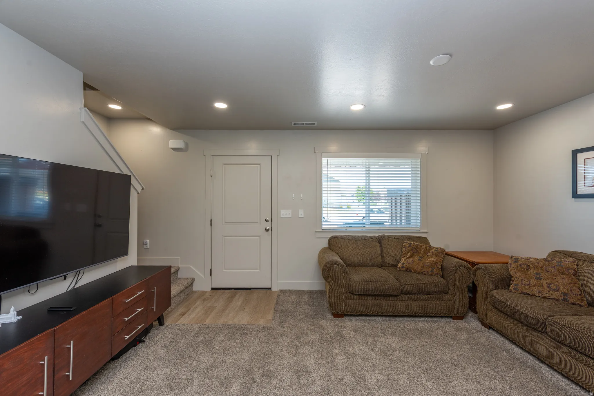 Spacious recreation room featuring recessed ceiling lighting, wood-finish flooring, and a media wall with mounted flat-screen television above wood cabinetry
