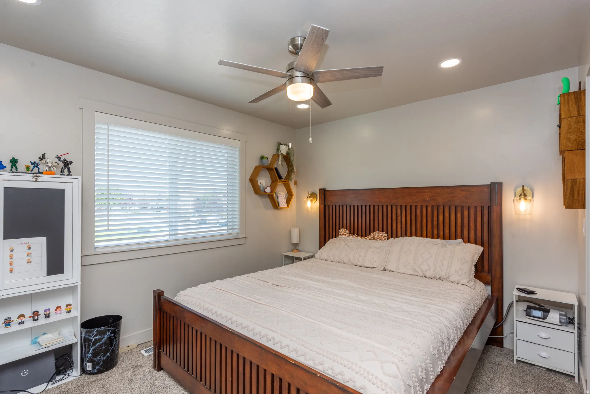 Carpeted bedroom featuring a large window with blinds, a ceiling fan with integrated lighting, recessed lighting, and wall-mounted sconces