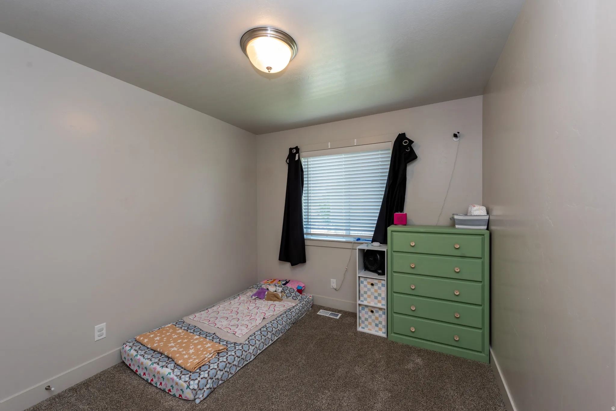 Neutral-toned room featuring a single window with blinds, a flush-mount ceiling light, and wall-to-wall carpeting