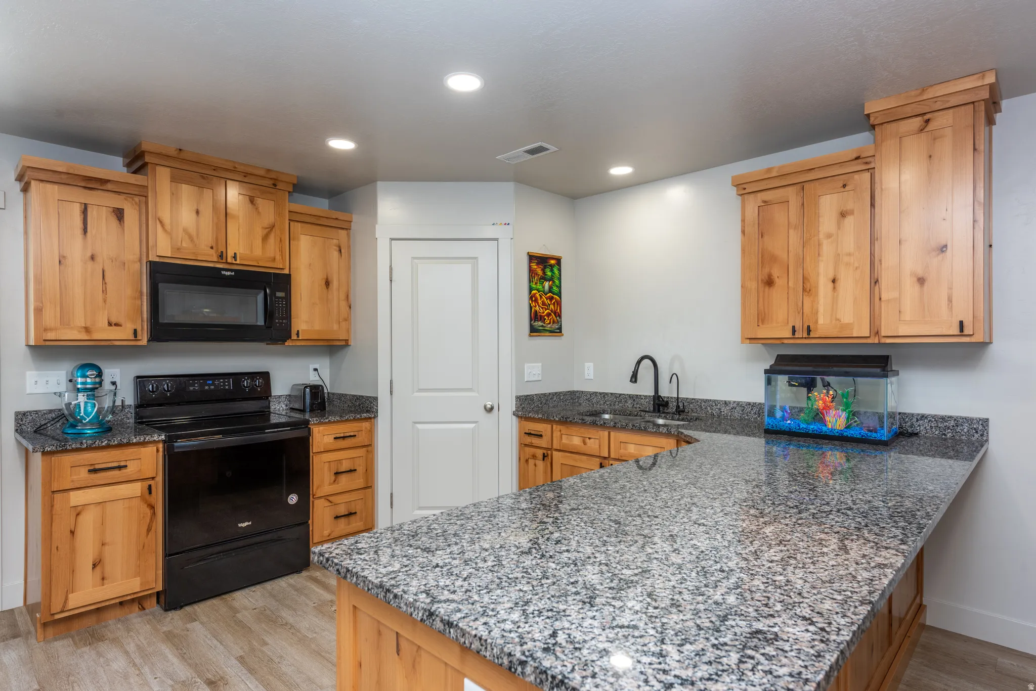 Kitchen featuring wood-finish cabinetry, granite countertops, black appliances, recessed lighting, and wood-finish flooring