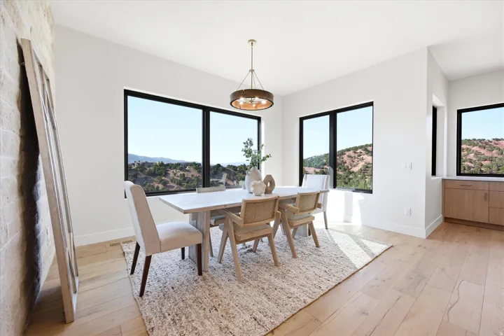 Spacious dining area featuring large windows, wood-finish flooring, a contemporary chandelier, and built-in cabinetry with a countertop