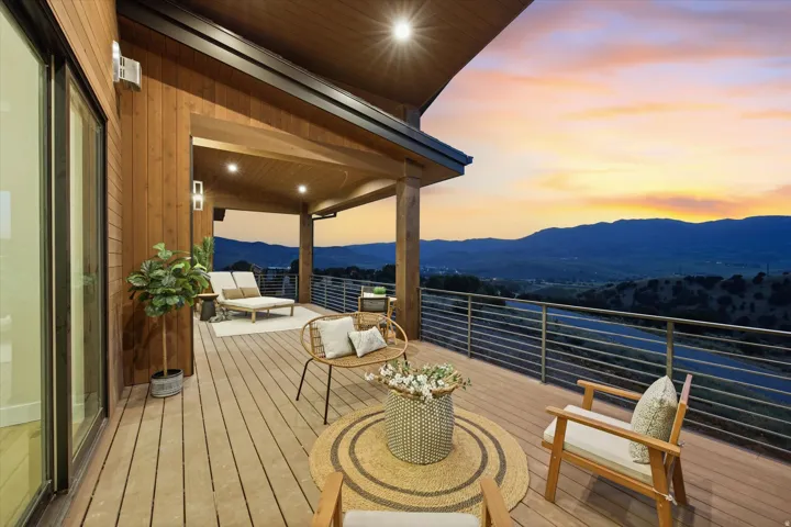Expansive outdoor deck with wood-finish flooring, featuring a covered area with recessed lighting, and a horizontal bar railing