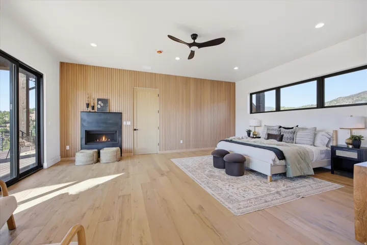 Wood-finish flooring with a linear wood-paneled accent wall, built-in fireplace, ceiling fan, and black-framed sliding glass doors opening to an outdoor deck