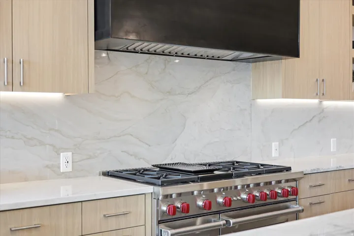 Gourmet kitchen featuring a stainless steel range with red accent knobs, a dark metal range hood, and light wood cabinetry with brushed nickel hardware