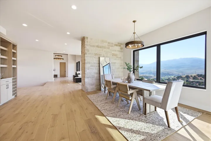 Spacious dining area featuring expansive windows, natural wood-finish flooring, recessed lighting, a built-in beverage bar, and a stone accent wall
