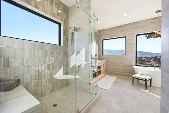 Glass-enclosed shower with a built-in bench, freestanding soaking tub, vanity with undermount sink, and large horizontal windows