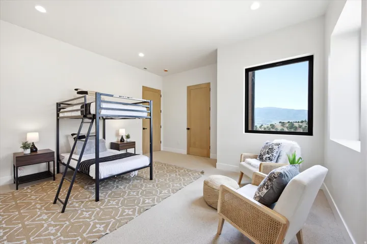 Bright secondary bedroom featuring a full bunk bed frame with integrated ladder, wood-finish flooring with geometric patterned area rug, recessed ceiling lighting, and a framed window with mountain backdrop