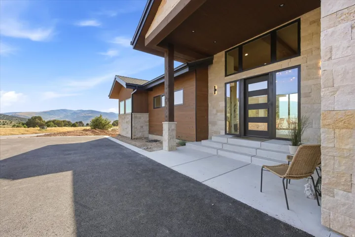 Modern architectural design featuring extensive stone and wood paneling, a contemporary entry door with glass panels, and multiple large windows