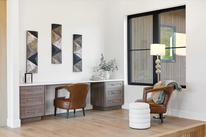 Sophisticated home office featuring a wood-finish desk with integrated storage, geometric wall art, and natural light from black-framed glass doors
