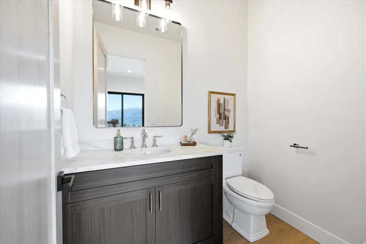 Spa-inspired bathroom featuring a dark wood-finish vanity with dual storage, white quartz countertop, polished nickel faucet and hardware, framed mirror with integrated lighting, white subway tile shower surround, and wood-finish flooring throughout