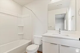 Bathroom featuring a white vanity with integrated sink, a rectangular mirror, a white toilet, and a white tub with shower surround